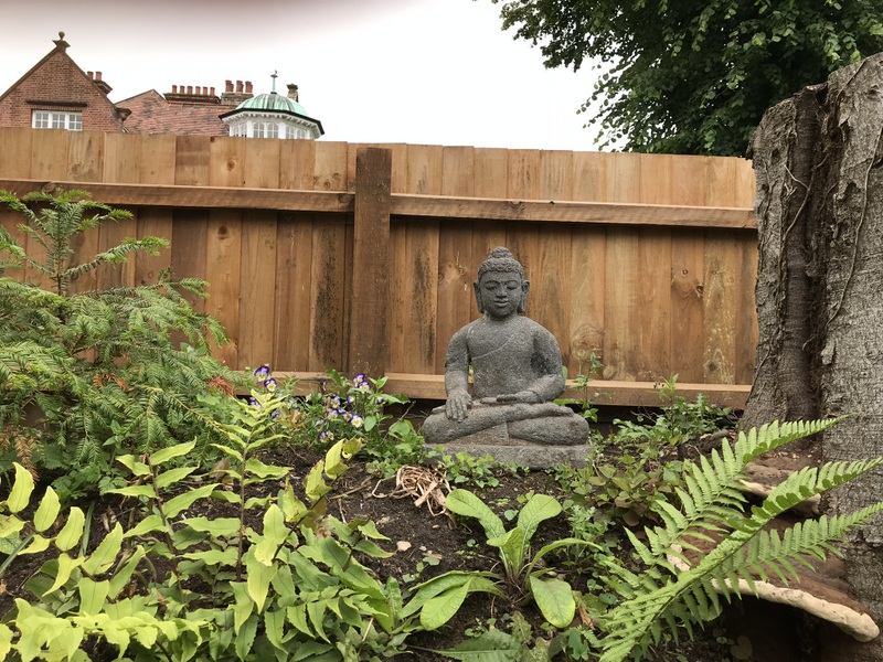 Stone Buddha statue in front of fence in garden