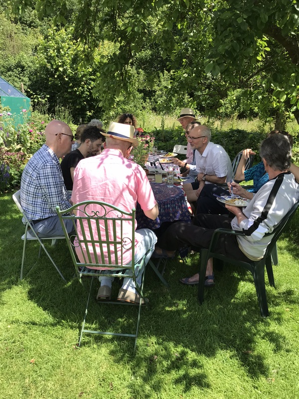 People sitting round a table eating outside in garden under a tree